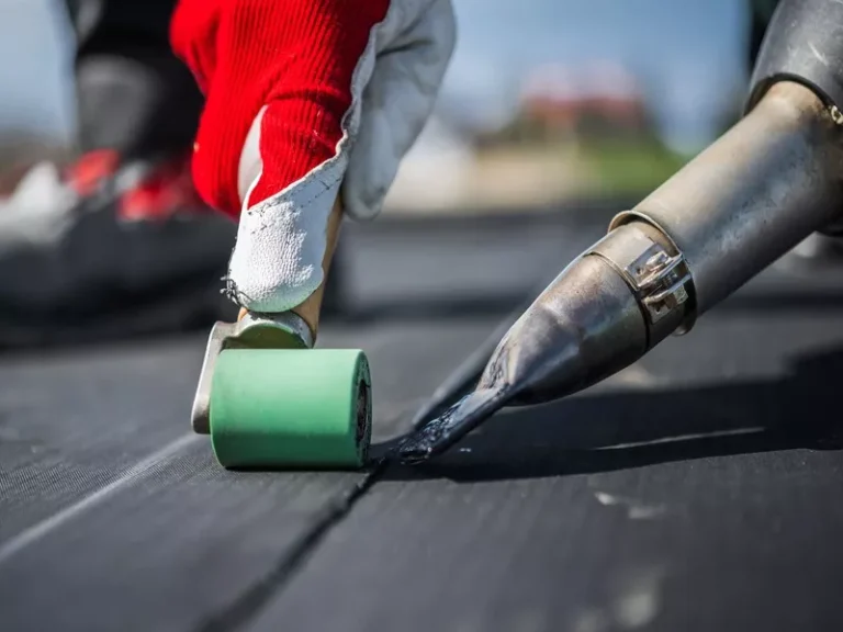Close-up of a roofer using a seam roller and specialized sealant to repair a puncture in a black EPDM flat roof.