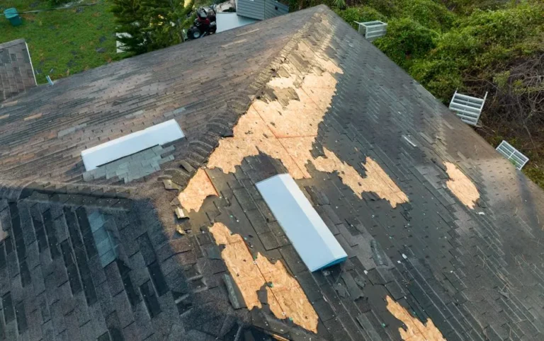 Aerial view of a residential roof with missing shingles and exposed plywood in need of urgent repair.
